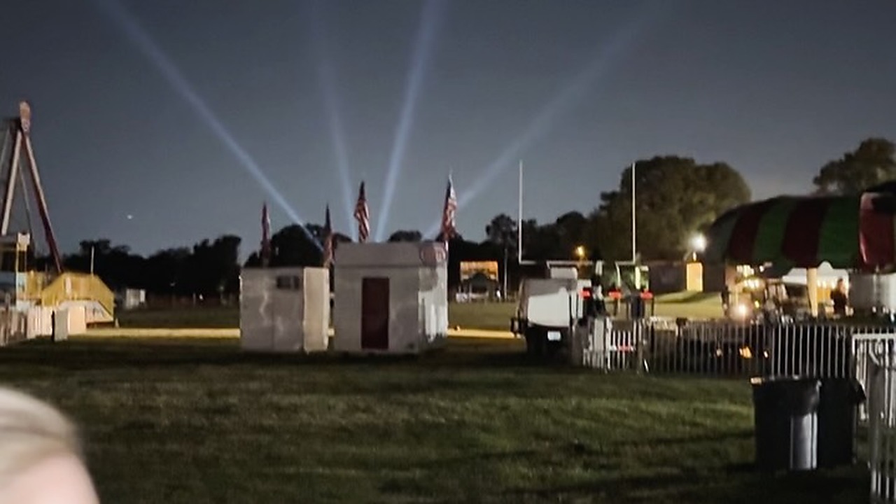 Four xenon beams towering above festival flags and carnival rides at night